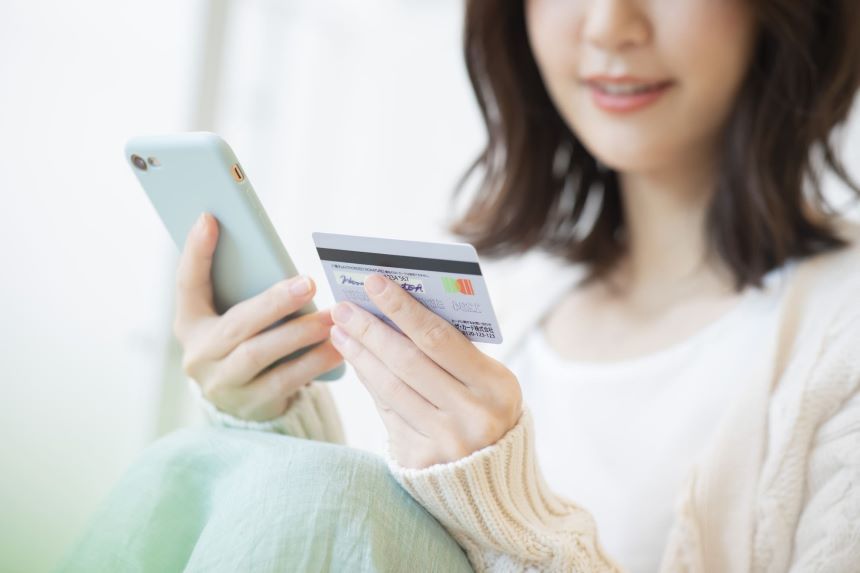 クレジットカードを見ながらスマホを操作する女性