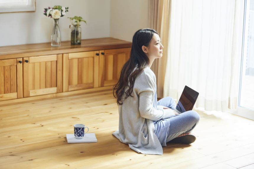 シンプルな部屋でパソコンを膝に乗せるキャッシュレスでミニマリストな女性