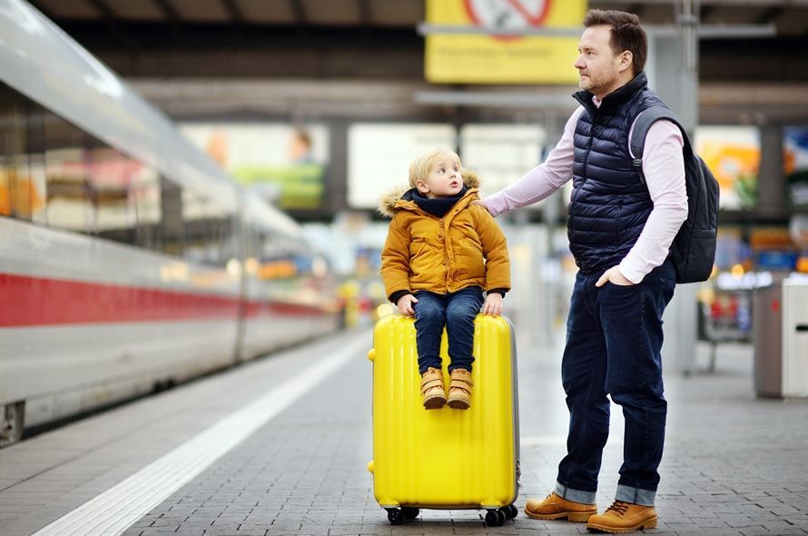 電車のホームでキャリーに乗っている子供とその父親