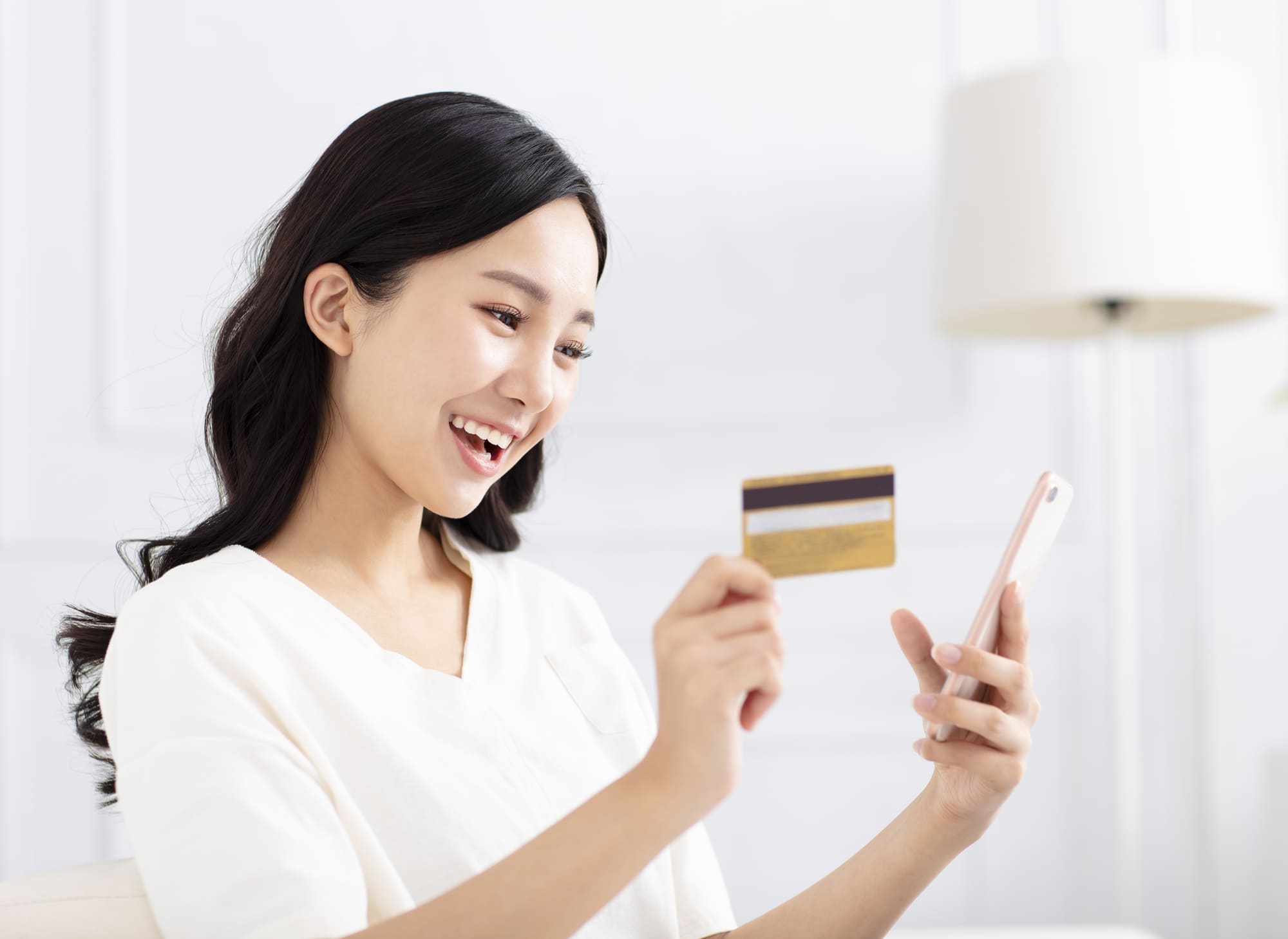 カードとスマホを持って喜ぶ白い服を着た女性