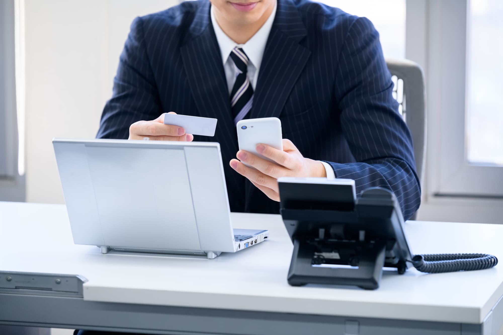 パソコン前でクレジットカードとスマホを手にするスーツ姿の男性