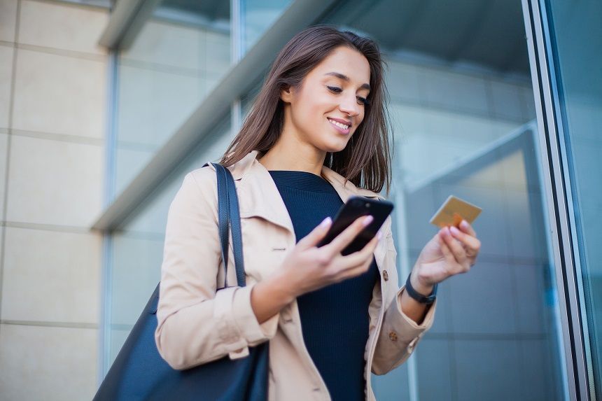 外出先でスマホとゴールドカードをもってほほ笑む女性