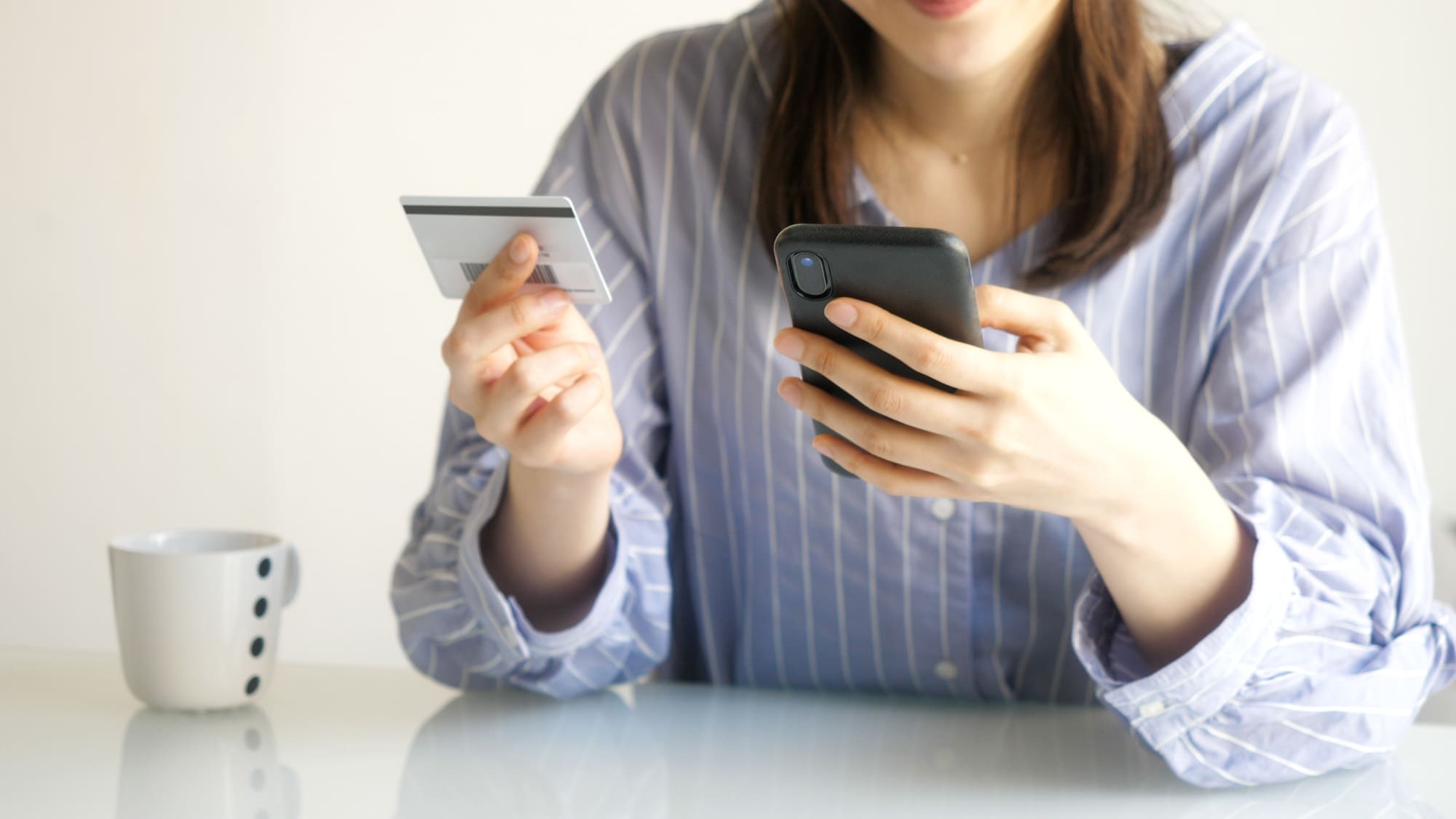 クレジットカード片手にスマホを操作する女性