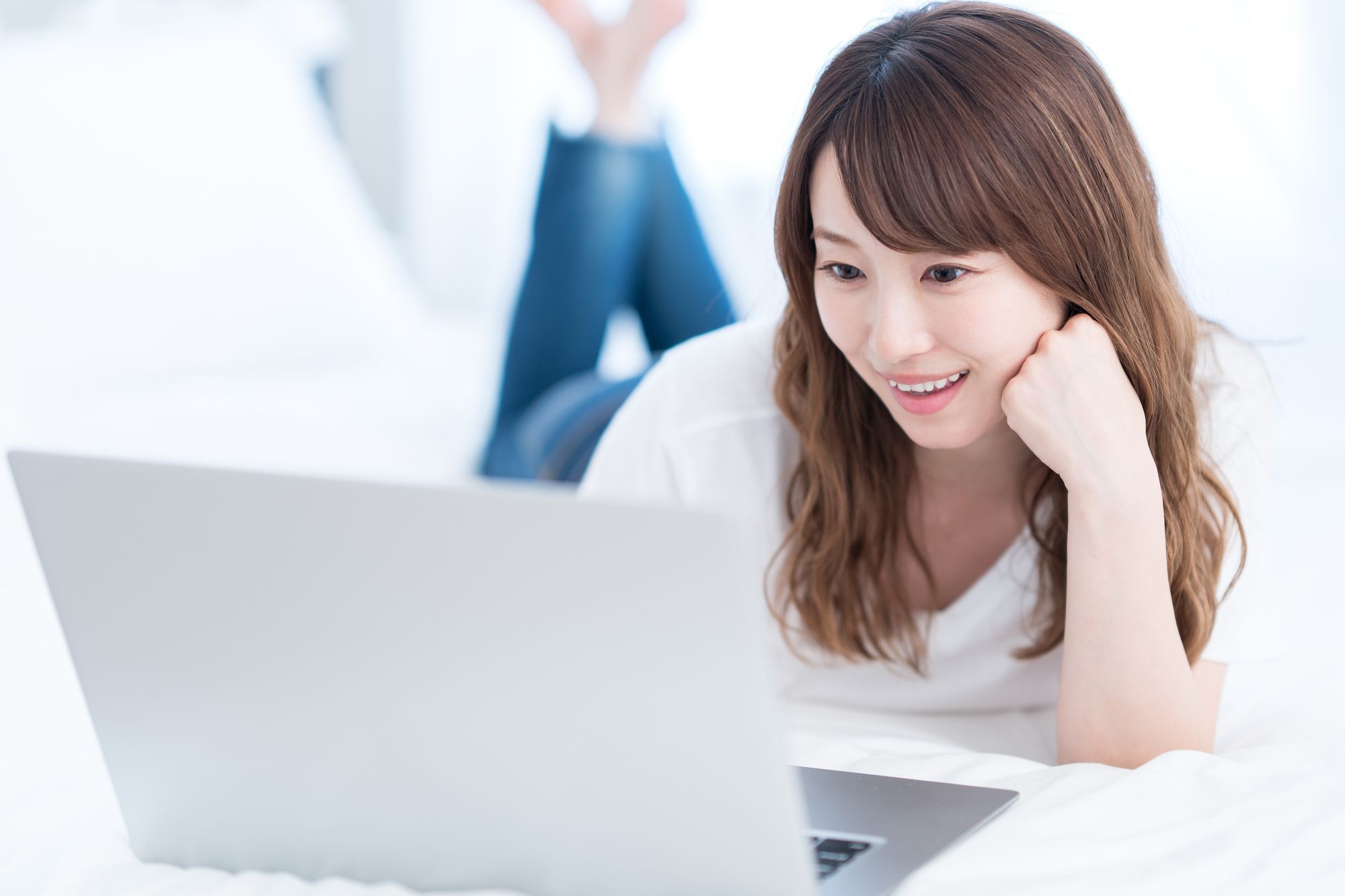 寝転びながらパソコンをみて微笑む女性