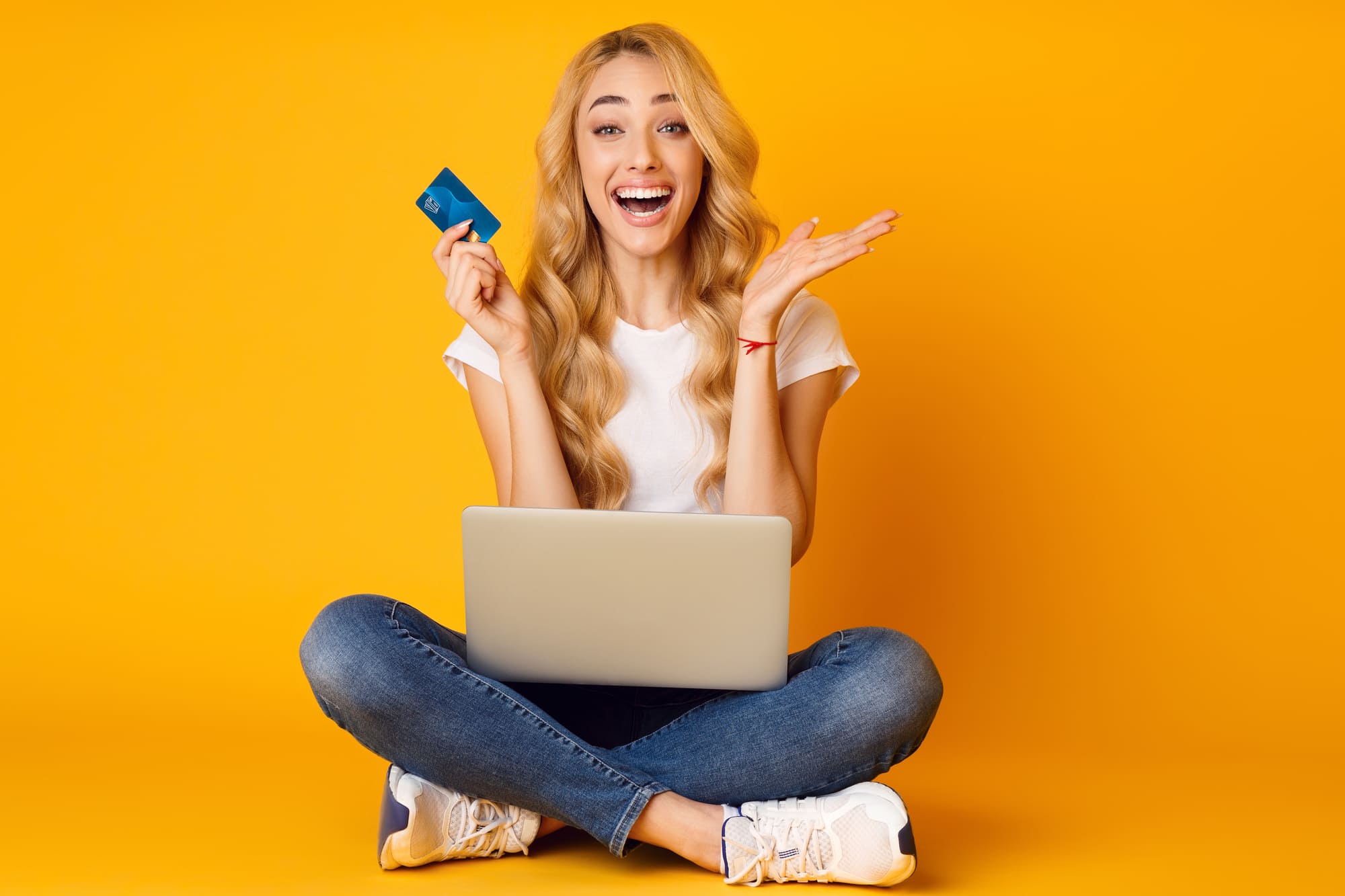 ノートパソコンの前で喜びながらクレジットカードを持つ外国人女性