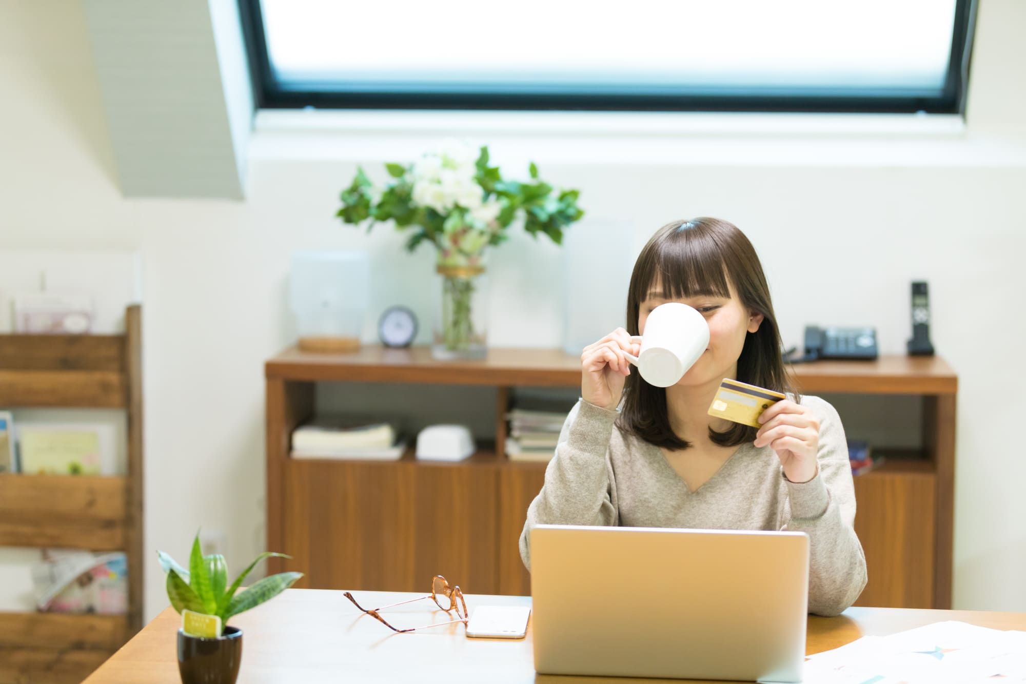 パソコンの前で飲みながらカードを見る女性
