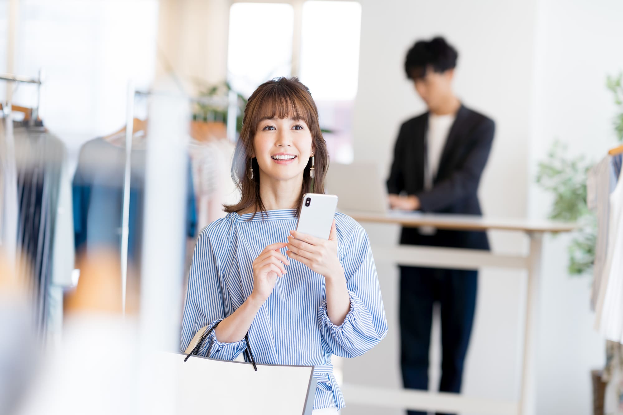 女性がスマホとショッピングバックを持って喜んでいる様子