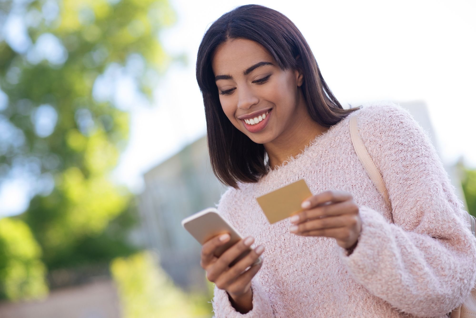 屋外でクレジットとスマホを見て微笑む女性