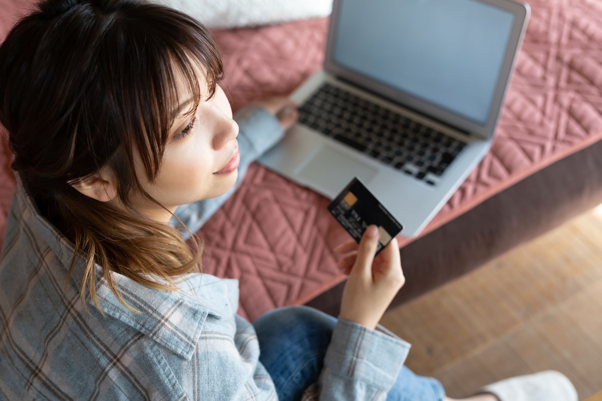 女性がパソコンを開きながらクレジットカードを持っている