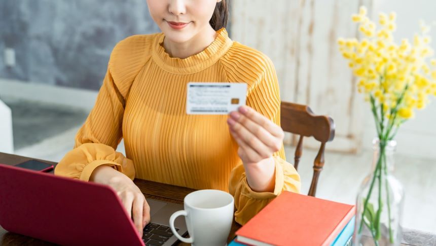 ノートパソコンの前でカードを見せる女性