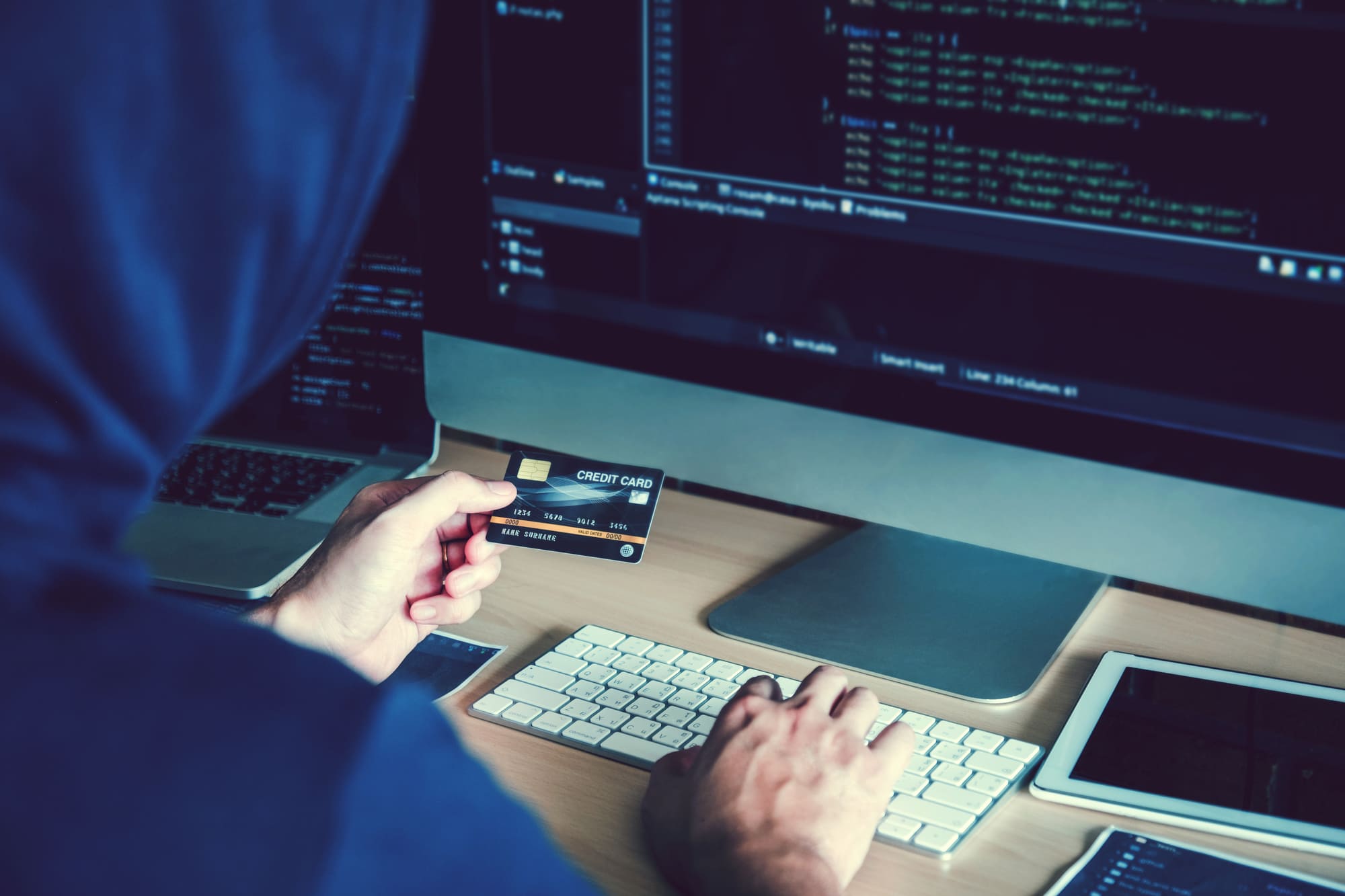 怪しい人がクレジットカードを見ながらパソコンを打つ様子