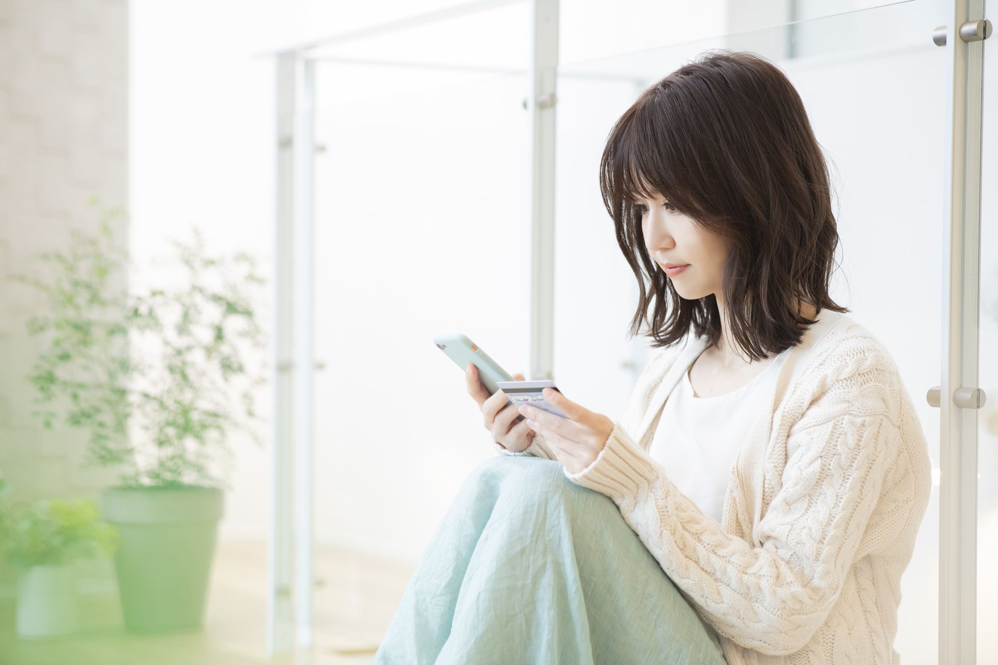 女性がスマートフォンとクレジットカードを見ている