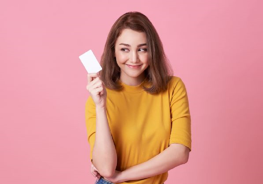 ピンクを背景にクレジットカードを持ち微笑む女性