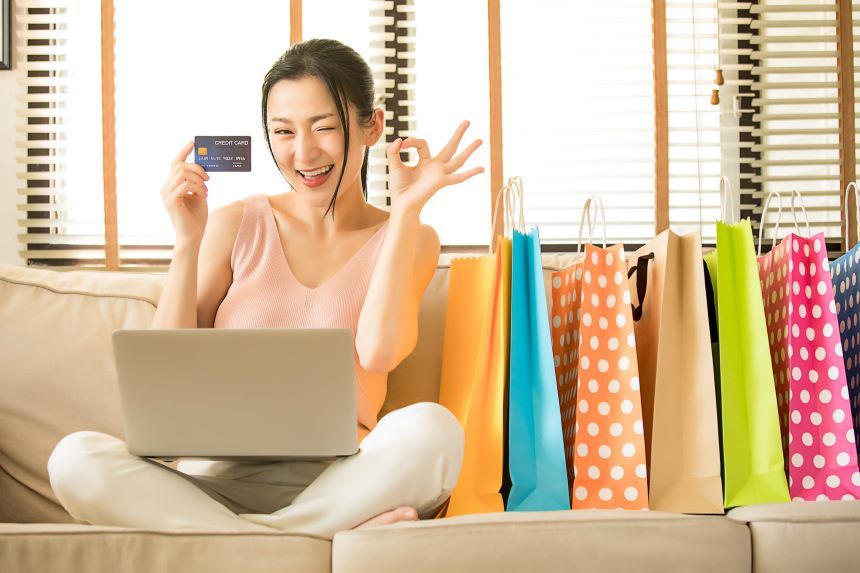 ショッピングバック横でクレジットカードを持ちOK サインをする女性