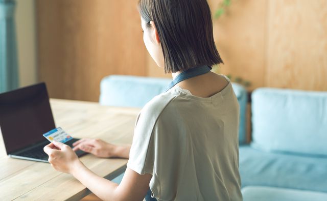 エプロンをつけた女性がクレジットカードを持ちながらパソコンを見ている