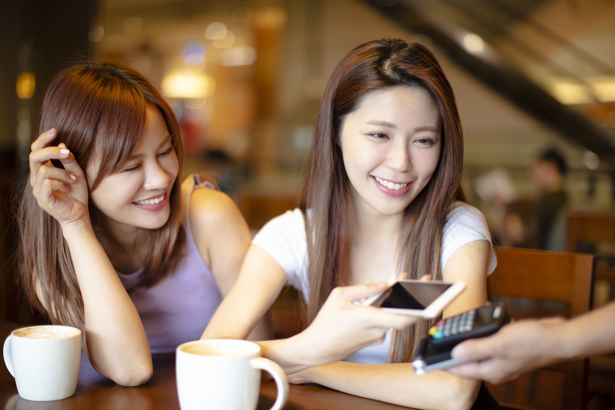女性二人がコーヒーショップでスマホのキャッシュレス決済