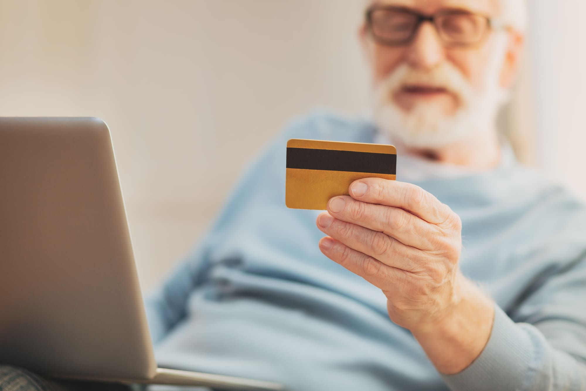 パソコンの前でデビットカードをみる老人男性